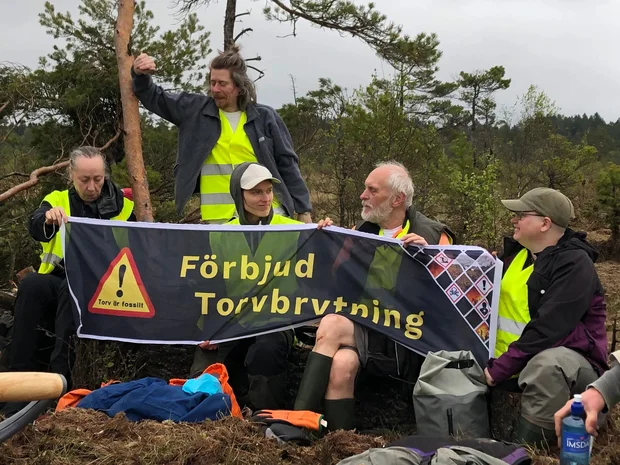 En grupp människor vid en torvbrytning som håller en banner "Förbjud torvbrytning"