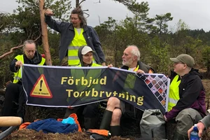 En grupp människor vid en torvbrytning som håller en banner "Förbjud torvbrytning"