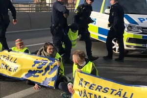 Aktivister med banner, delvis fastlimmad med polis i bakgrund