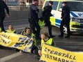 Aktivister med banner, delvis fastlimmad med polis i bakgrund