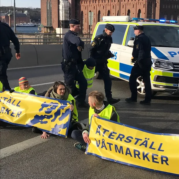 Aktivister med banner, delvis fastlimmad med polis i bakgrund