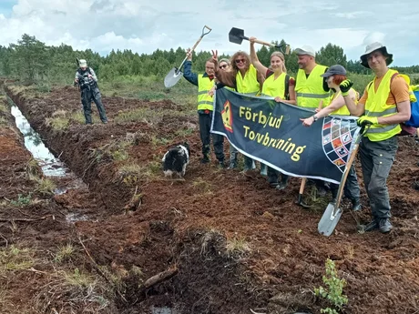 Människor som håller an banner från Återställ Våtmarker bakom en igenpluggad dike
