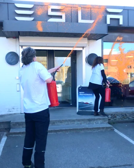 Aktivist från Återställ Våtmarker sprayar Tesla byggnad med orange färg.