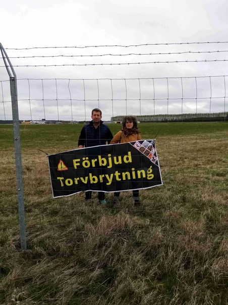 Aktivister bakom staketet av Trollhättans flygplatsen med en banner som kräver slutet av torvbrytningen.