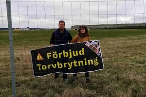 Activists behind the fence at Trollhättan Airport with a banner demanding an end to peat extraction.