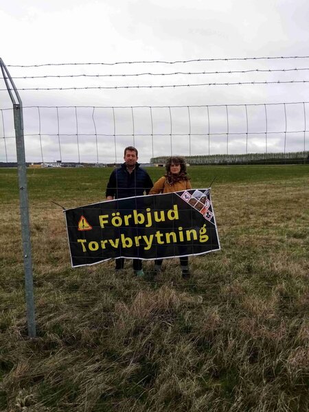Aktivister bakom staketet av Trollhättans flygplatsen med en banner som kräver slutet av torvbrytningen.