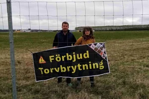 Aktivister bakom staketet av Trollhättans flygplatsen med en banner som kräver slutet av torvbrytningen.