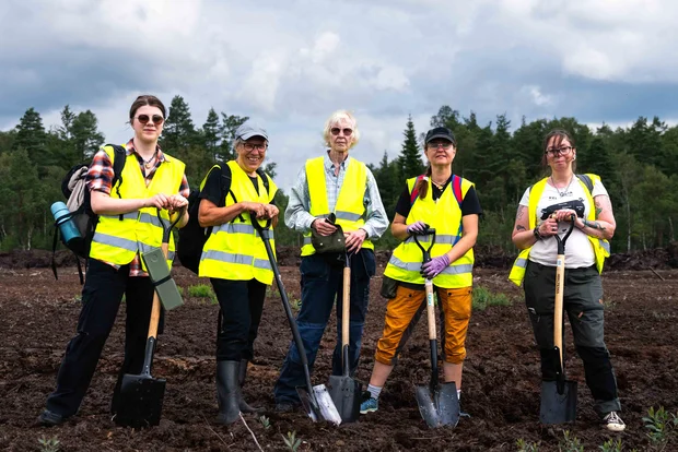 Fyra aktivister klädda i gul reflexväst. De är glada och har spadar i hand. Står på Grimsås mosse