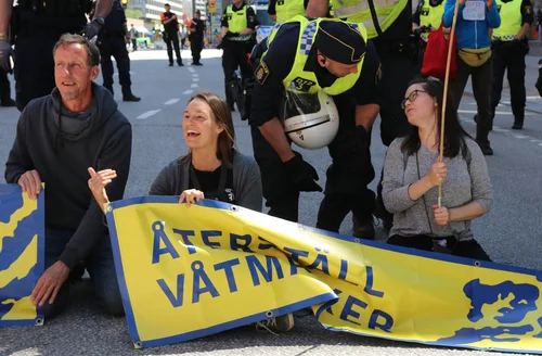 Energetiska människor som protesterar för återställning av våtmarker med en blockad av en gata, en polisman pratar med en av aktivisterna.