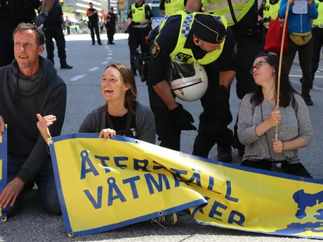 Energetiska människor som protesterar för återställning av våtmarker med en blockad av en gata, en polisman pratar med en av aktivisterna.
