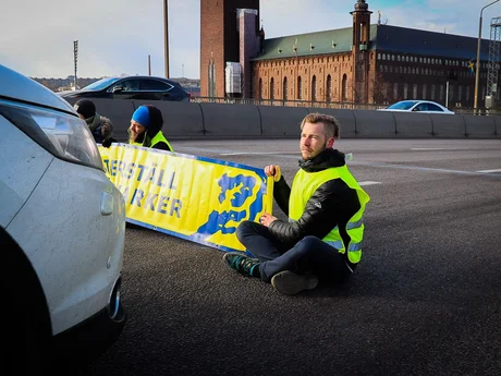 Aktivist som blockerar en väg och håller en banner; direkt framför personen en skåpbil.