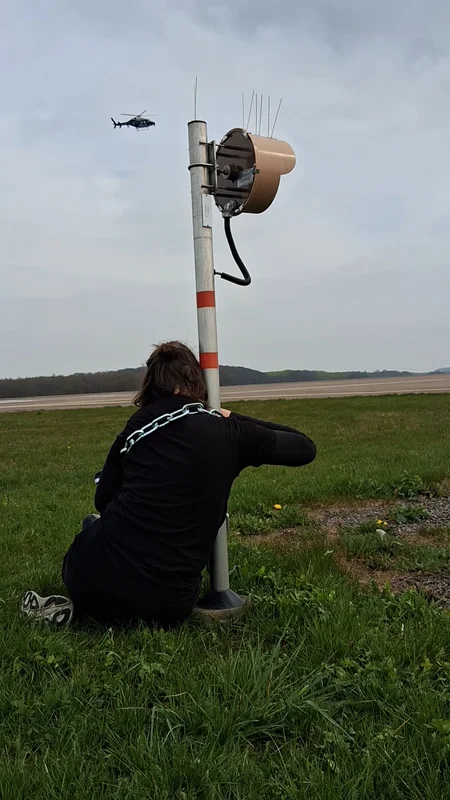 En aktivist från Återställ Våtmarker låst på en stolpe på flygplatsen Malmö Airport med en flygande helikopter i bakgrunden.