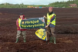 Två människor från Återställ Våtmarker på en mosse som håller en banner "Förbjud torvbrytning"