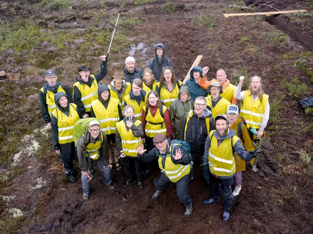 Grupp av människor med gula västor på en mosse i aktion mot torvbrytning, fotograferad från en drönare