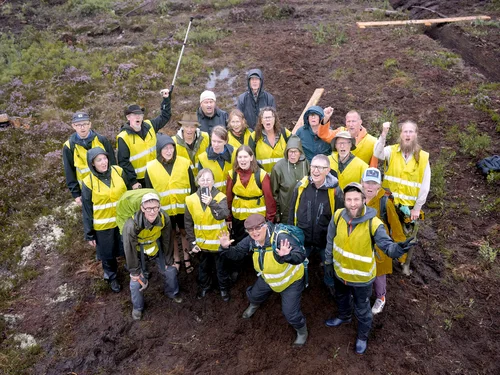 Grupp av människor med gula västor på en mosse i aktion mot torvbrytning, fotograferad från en drönare