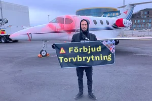 Människa med en banner "Förbjud torvbrytning" framför ett flygplan som färgades delvis röd.