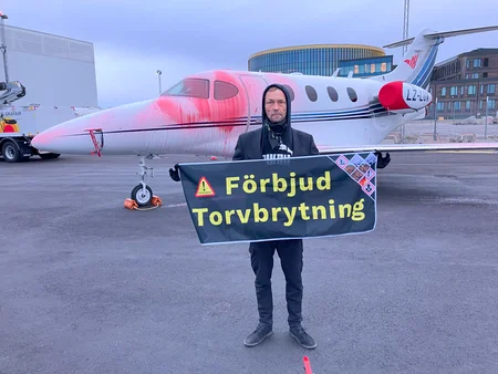 Människa med en banner "Förbjud torvbrytning" framför ett flygplan som färgades delvis röd.