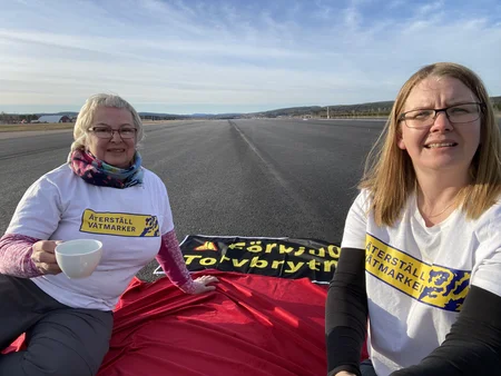 Två kvinnor som sitter på landningsbana av Sundvalls flygplats som demonstration mot torvbrytning i Sverige.