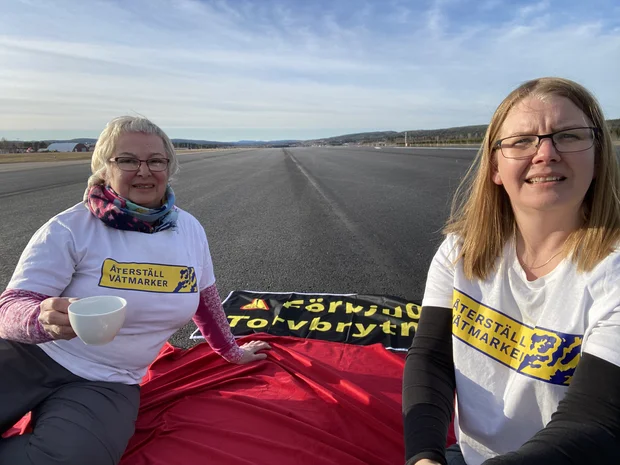 Två kvinnor som sitter på landningsbana av Sundvalls flygplats som demonstration mot torvbrytning i Sverige.