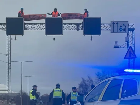 Aktivister på ställning med trafikmärke ovanför en motorväg, polisbild i förgrund
