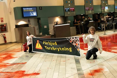 Aktivister från Återställ Våtmarker håller en banner efter de färgarde golvet röd i hallen av flygplats Landvetter