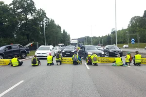 People from Återställ Våtmarker (Restore Wetlands) are sitting on the street, blocking it in such a way that cars have to stop.