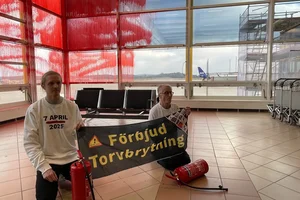Två aktivister från Återställ Våtmarker i terminalen av flygplatsen i Malmö, rördfärgade fönster i bakgrunden.