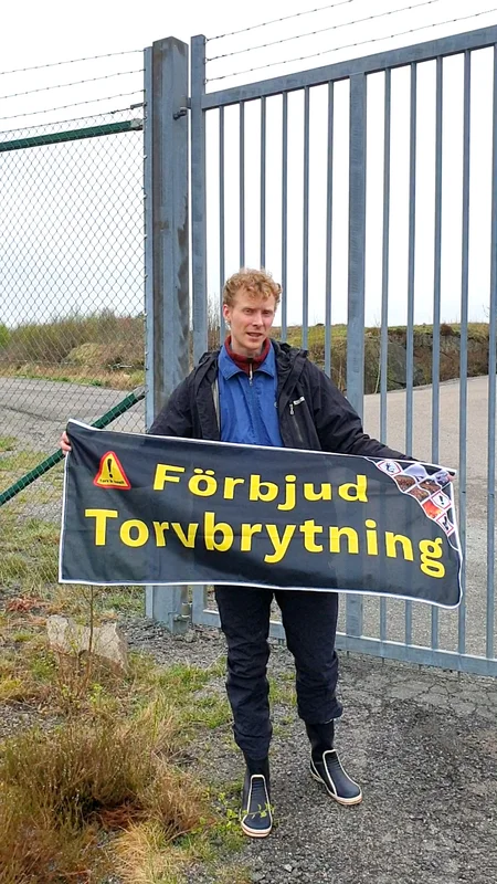 Aktivist från Återställ Våtmarker som håller en banner "Förbjud torvbrytning" i samband med aktionen på flygplatsen i Landvetter.